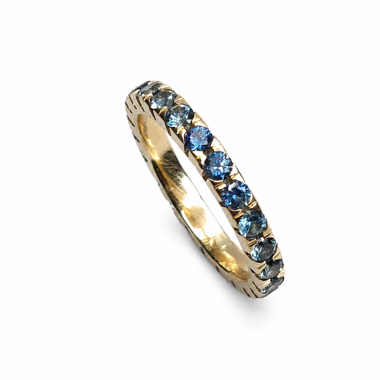 Handmade 14K yellow gold eternity band featuring 2.30 carats of blue Montana sapphires arranged in a continuous colour gradient.